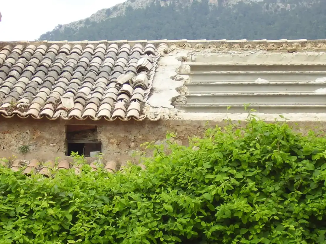 Tejado de teja árabe envejecido sobre un muro de piedra. Impermeabilización de cubiertas y tejados en León
